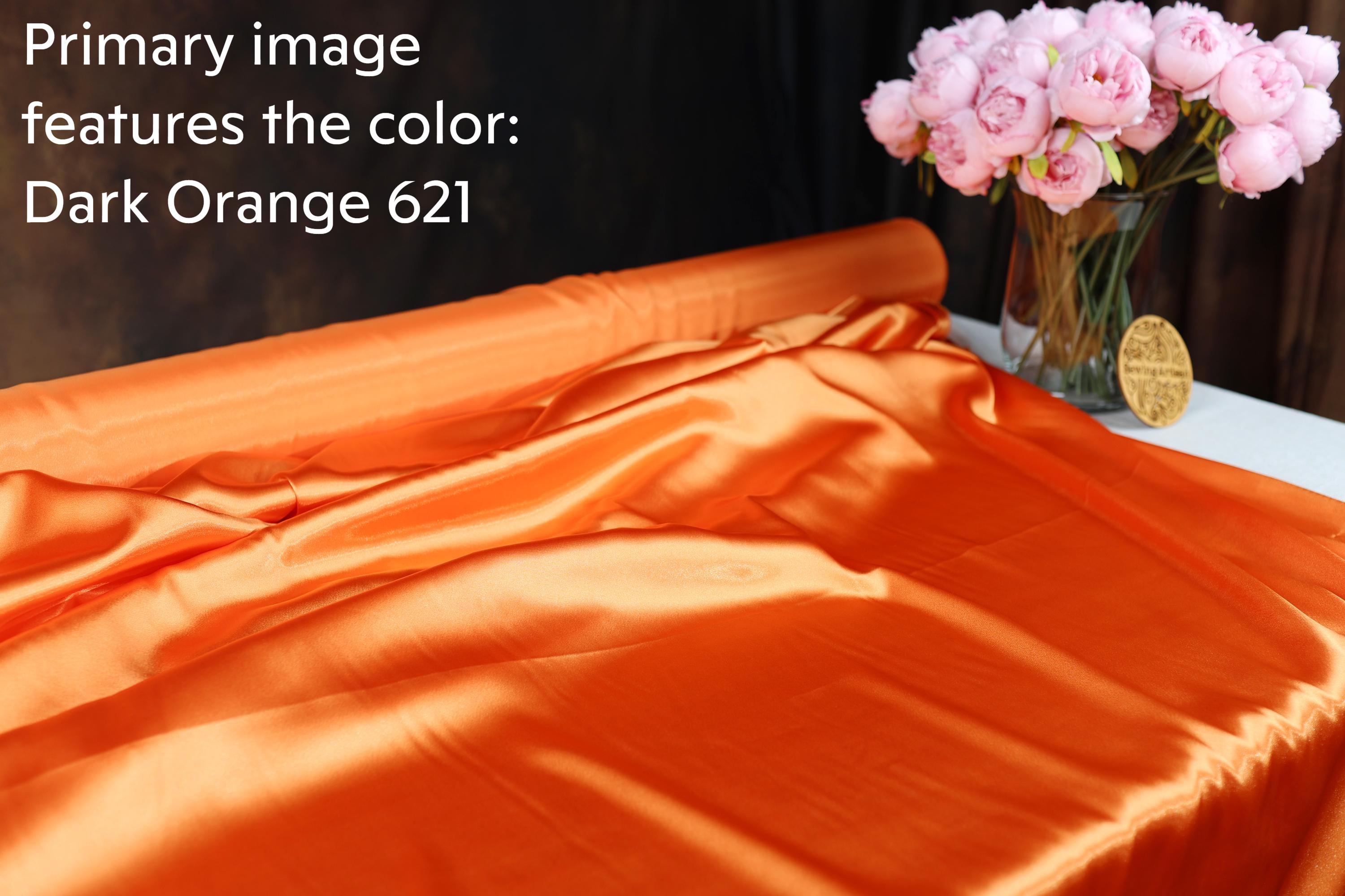 a dark orange fabric with a vase of pink flowers on a table.