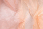 The image is a close-up of a fabric with a light peach or peach-colored texture, adorned with small, glittery particles or specks that create a sparkling effect.