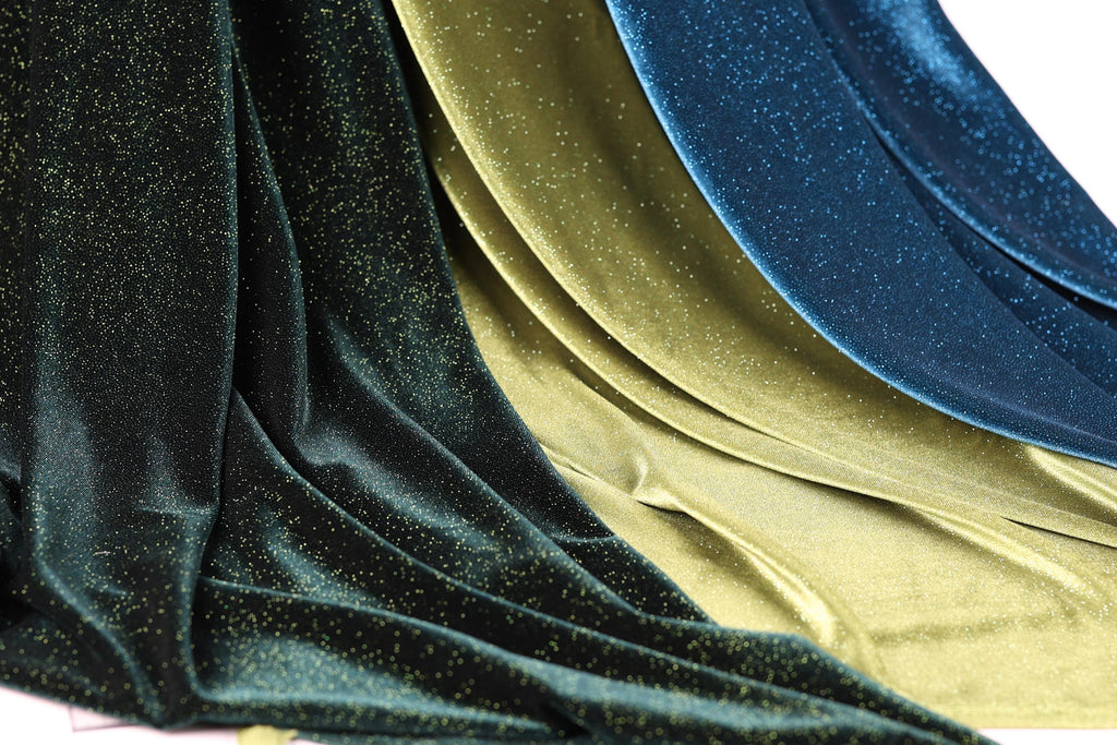 a close-up view of a fabric with a shimmering gold and blue glittery texture. The fabric appears to be made of a shiny material, possibly silk or velvet, and has a flowing, draped appearance. The colors of the fabric are gold and blue, creating a visually striking contrast.