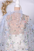 a close-up view of a delicate, sheer fabric with a floral pattern. The fabric appears to be made of sheer material, giving it a delicate and airy appearance. The floral pattern is intricate and detailed, adding a touch of elegance to the fabric. The background of the image is plain white, which contrasts with the colorful floral pattern on the fabric.