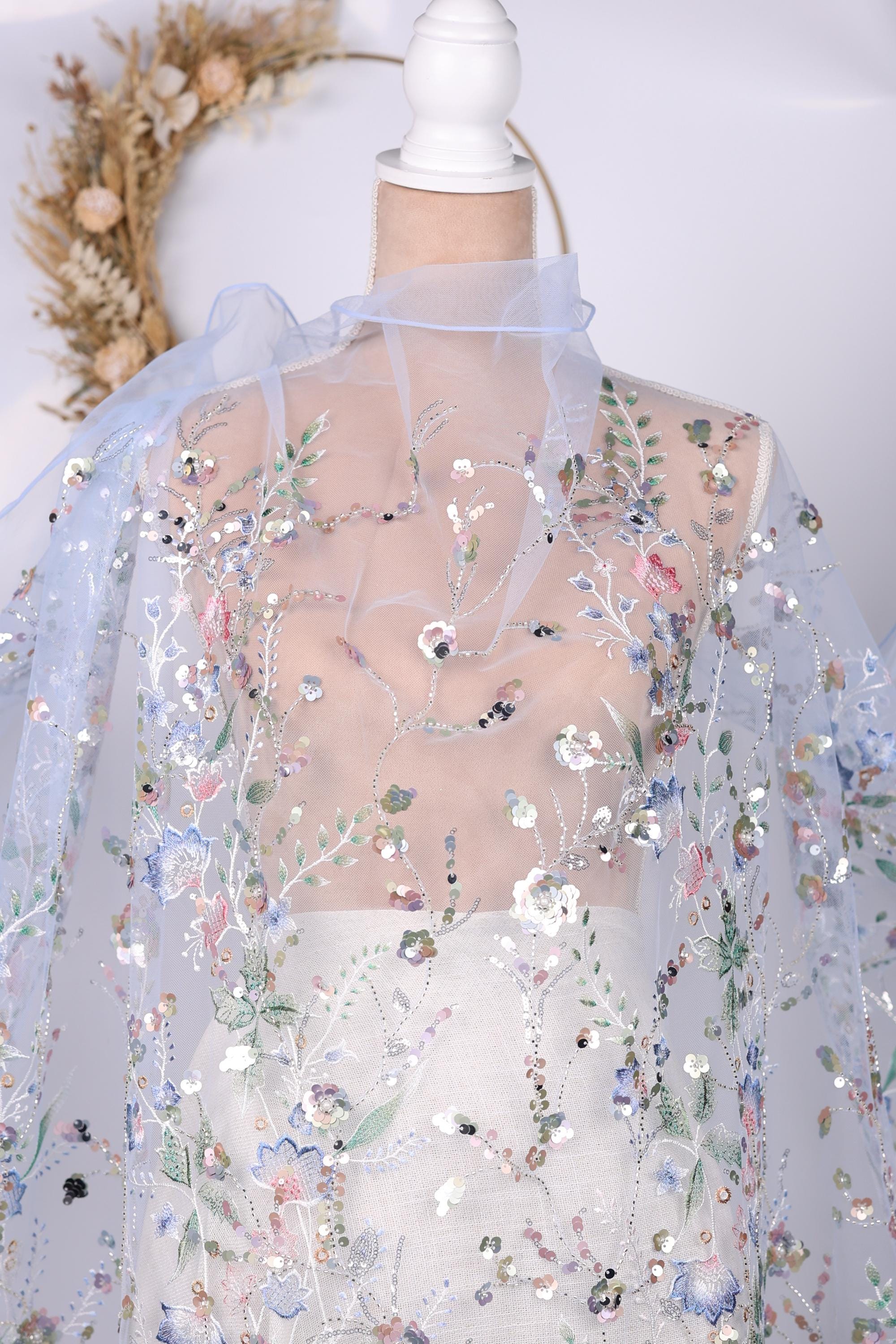 a close-up view of a delicate, sheer fabric with a floral pattern. The fabric appears to be made of sheer material, giving it a delicate and airy appearance. The floral pattern is intricate and detailed, adding a touch of elegance to the fabric. The background of the image is plain white, which contrasts with the colorful floral pattern on the fabric.