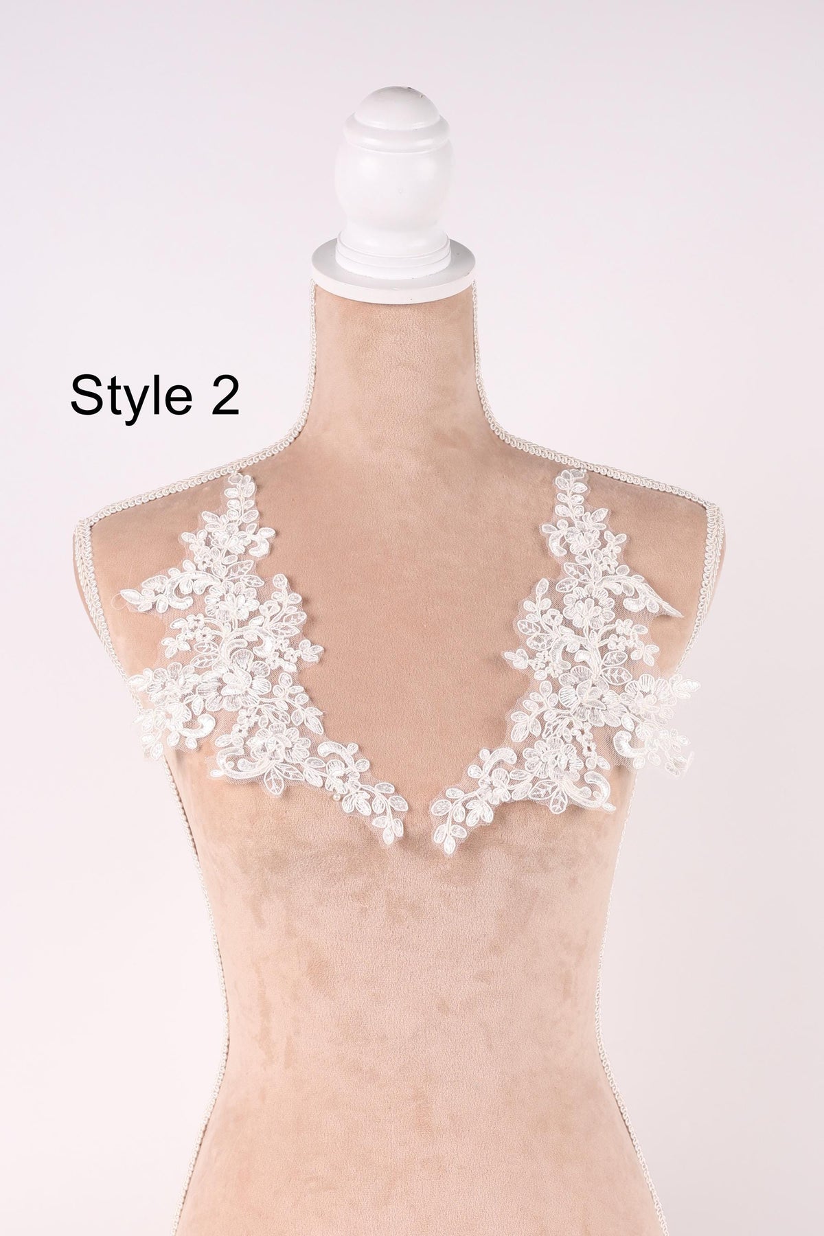 A mannequin wearing a white lace dress with a floral pattern on the shoulders.