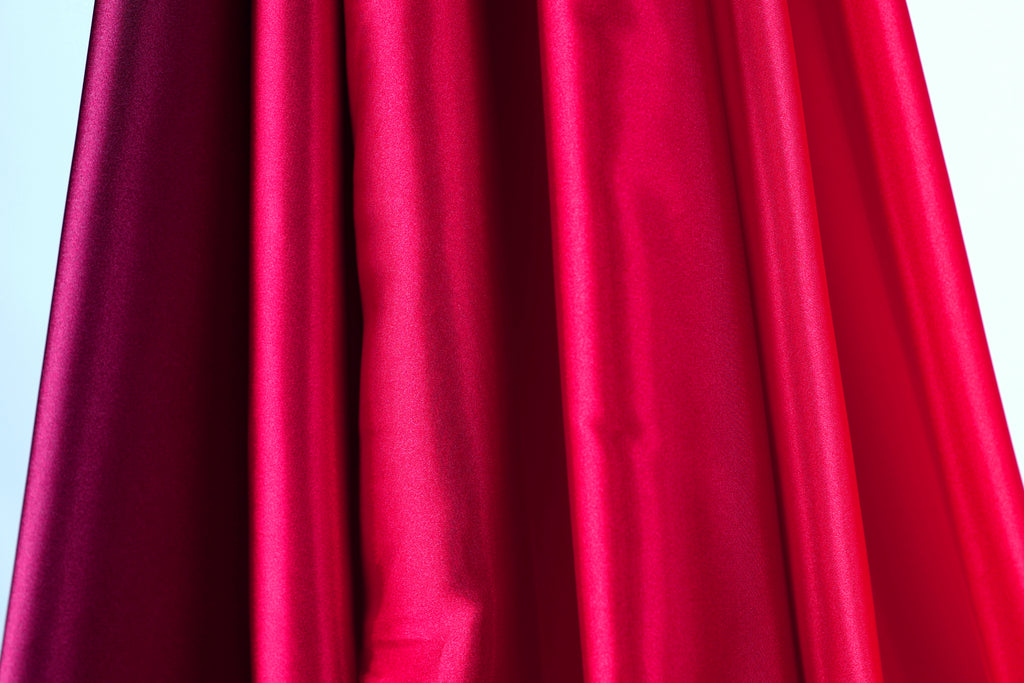 a close-up view of a red fabric, possibly a curtain or garment, with a dark red or burgundy hue. The fabric appears to be made of a shiny, smooth material, giving it a luxurious and elegant appearance.