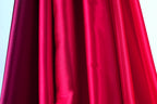 a close-up view of a red fabric, possibly a curtain or garment, with a dark red or burgundy hue. The fabric appears to be made of a shiny, smooth material, giving it a luxurious and elegant appearance.