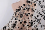 a close-up view of a delicate, sheer fabric with a black floral pattern. The fabric appears to be a sheer lace or chiffon material, with a floral design that includes black flowers and leaves. The fabric is displayed against a plain white background, which highlights the intricate details and textures of the fabric.