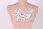 a mannequin with a delicate, intricate embroidered design on its bust. The design is a floral pattern with white and light blue elements, creating a visually appealing and elegant appearance.