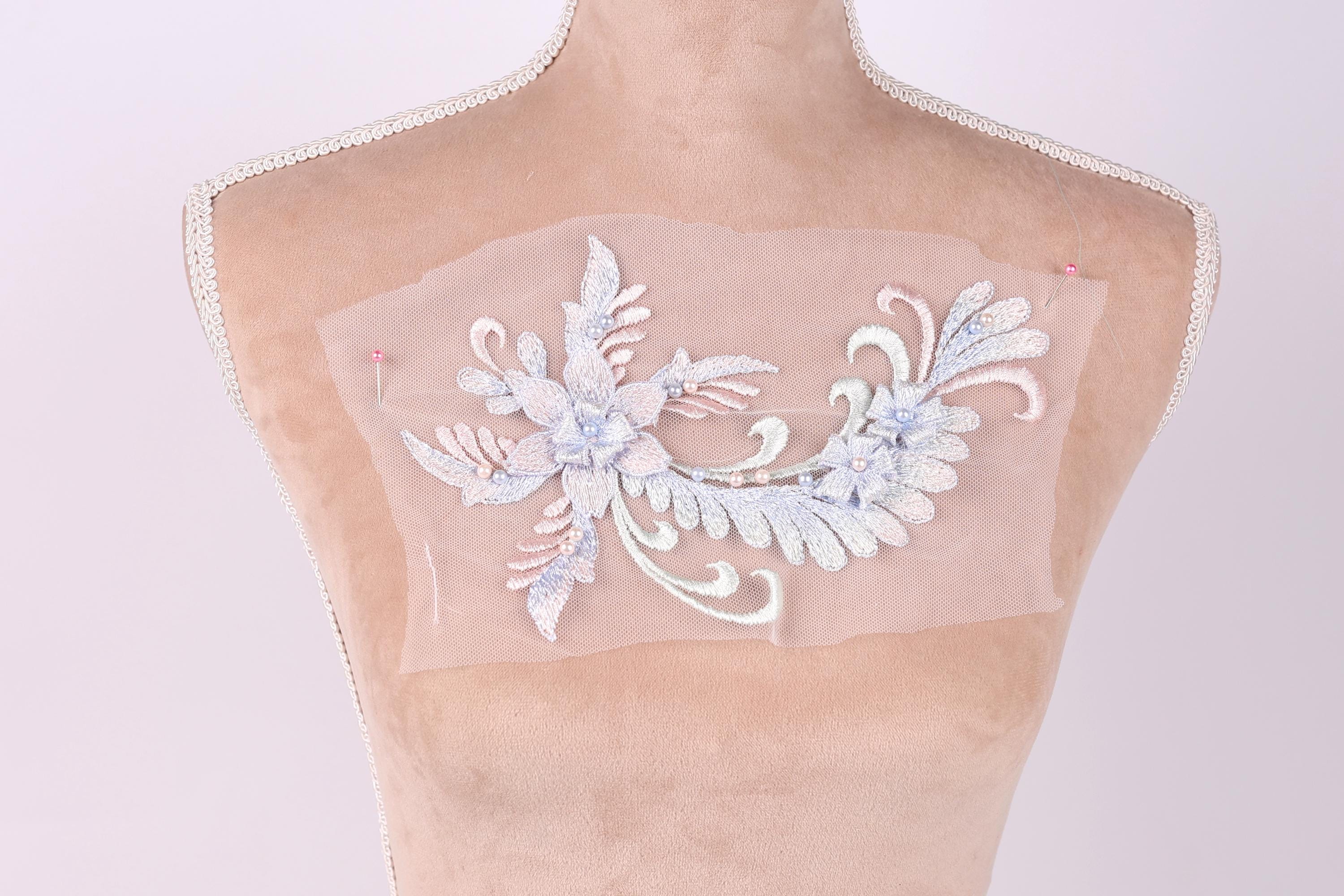 a mannequin with a delicate, intricate embroidered design on its bust. The design is a floral pattern with white and light blue elements, creating a visually appealing and elegant appearance.