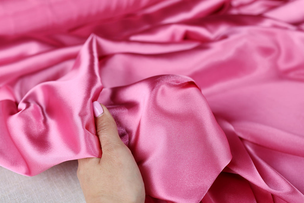 a person is holding a pink satin material