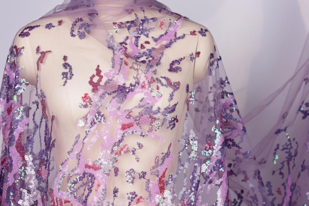 a mannequin wearing a sheer, purple, and pink sequin fabric draped over its body.