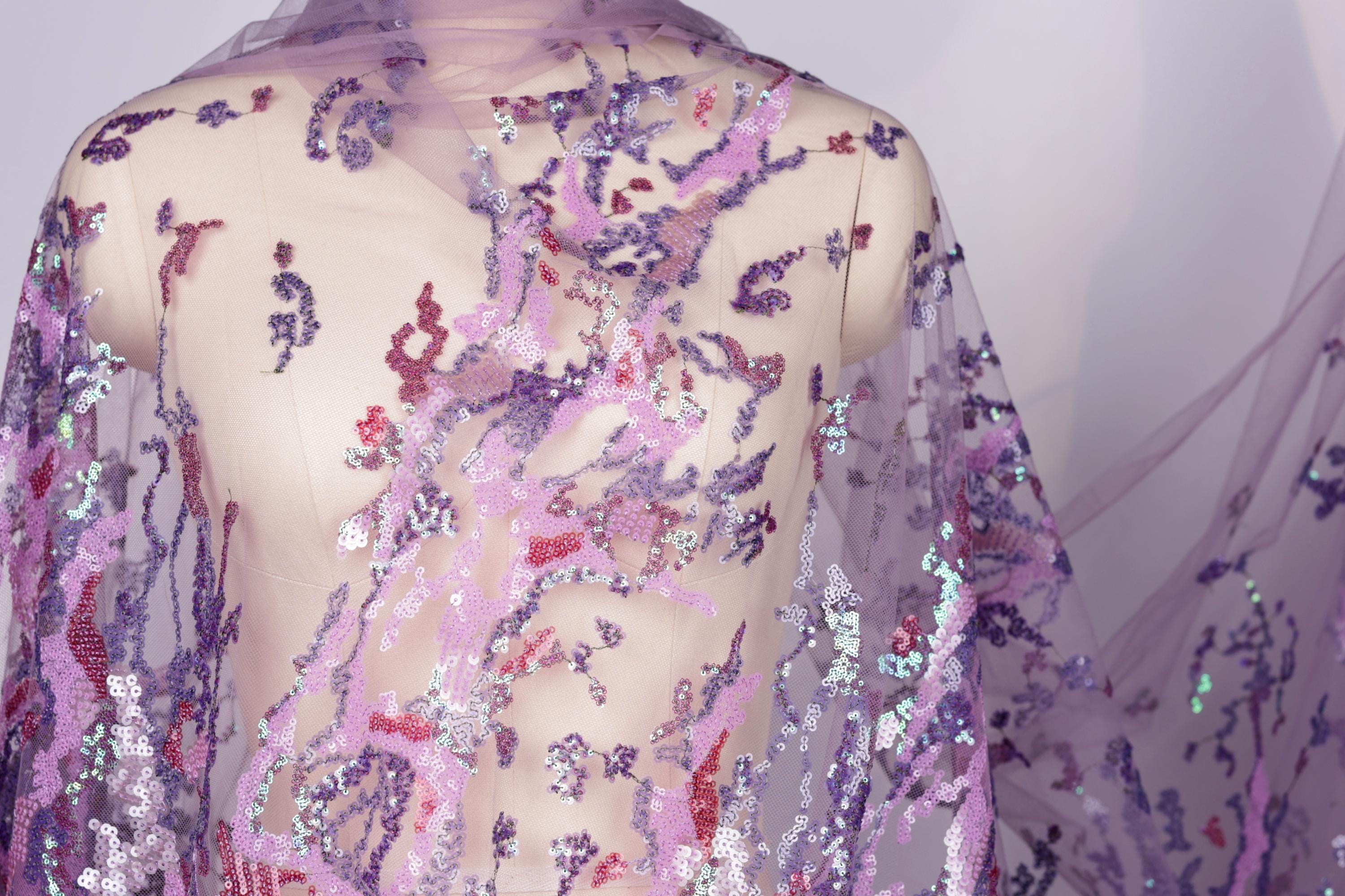 a mannequin wearing a sheer, purple, and pink sequin fabric draped over its body.