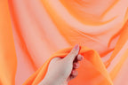 A hand is holding a piece of orange fabric, which appears to be a soft, flowing material.