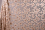 a close-up view of a fabric with a floral pattern, including small flowers and leaves. The fabric appears to be made of a light-colored material, possibly lace or a similar type of material. The pattern is intricate and detailed, with the flowers and leaves varying in size and shape. The image does not contain any text or other discernible objects, and the focus is solely on the floral pattern on the fabric.