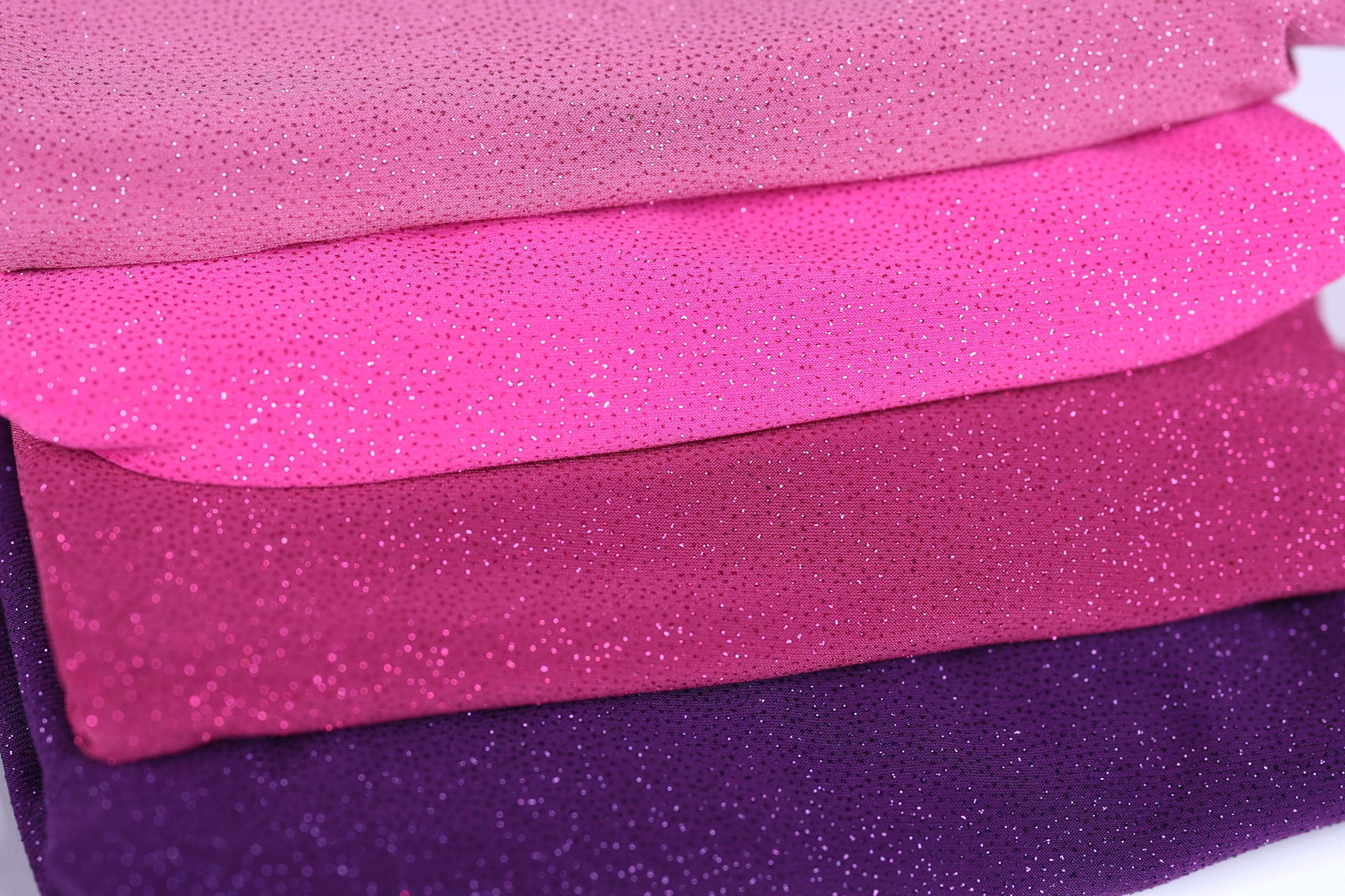 A close-up image of a pile of fabric with a glittery texture, featuring a variety of colors including pink, purple, and purple.