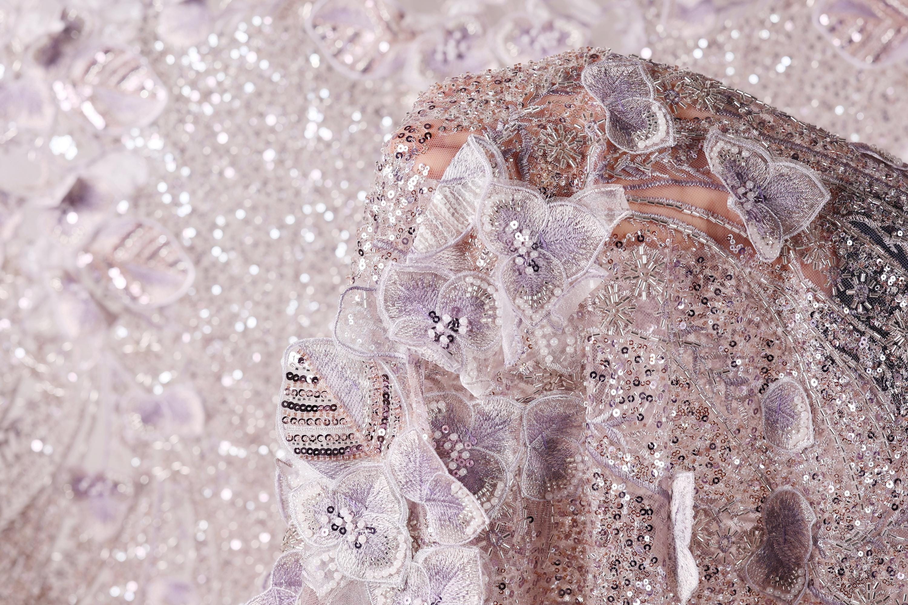 a close-up view of a delicate, intricately designed fabric with a floral pattern. The fabric is adorned with numerous small, sparkling sequins that add a touch of elegance and sophistication to the overall design. The close-up perspective allows for a detailed examination of the fabric's texture and the intricate patterns created by the sequins.