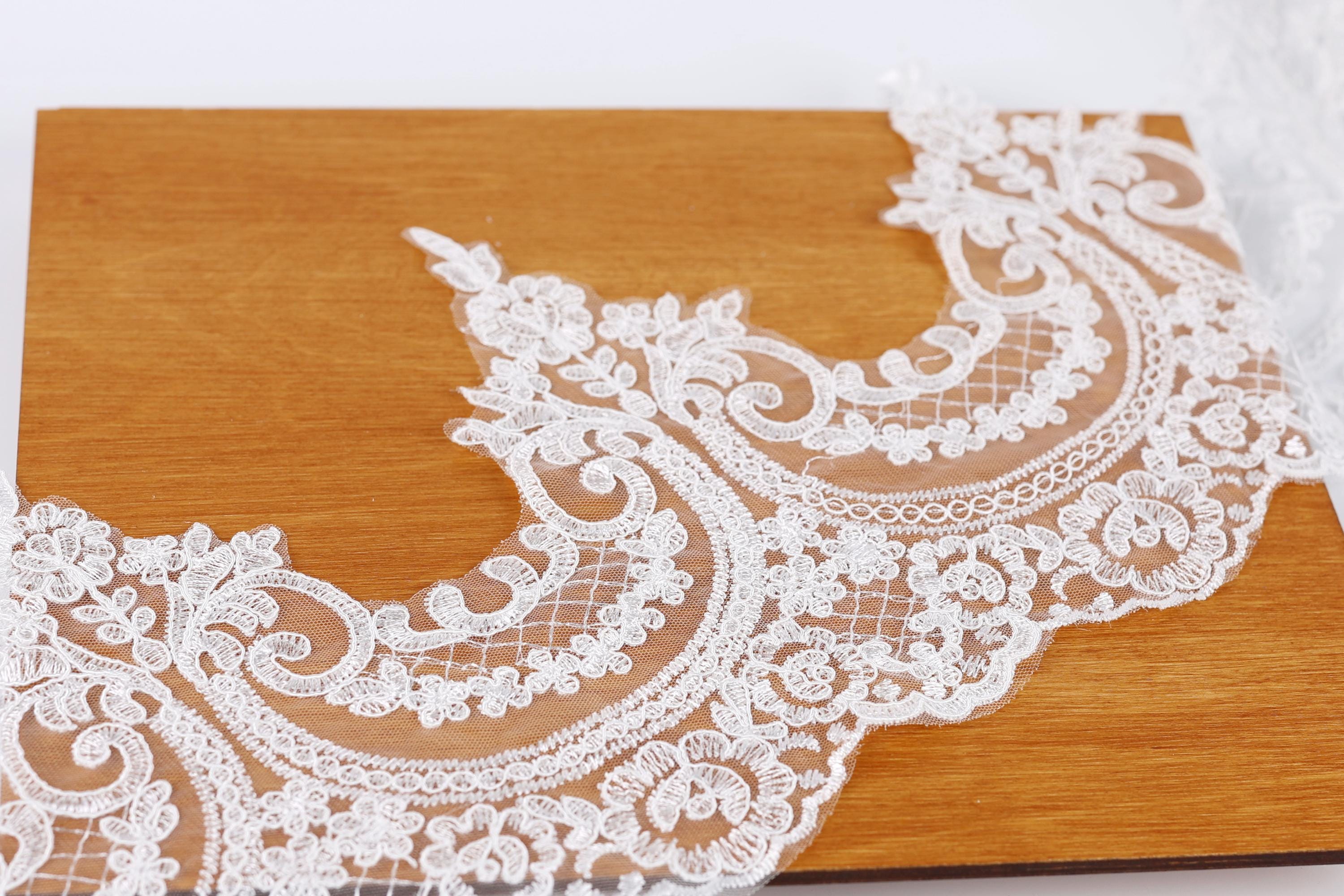 a close-up view of a delicate, intricate white lace fabric with a floral pattern, resting on a wooden surface.