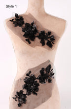A mannequin wearing a beige dress with black floral embellishments, including a large black flower and smaller black flowers, displayed on the dress.