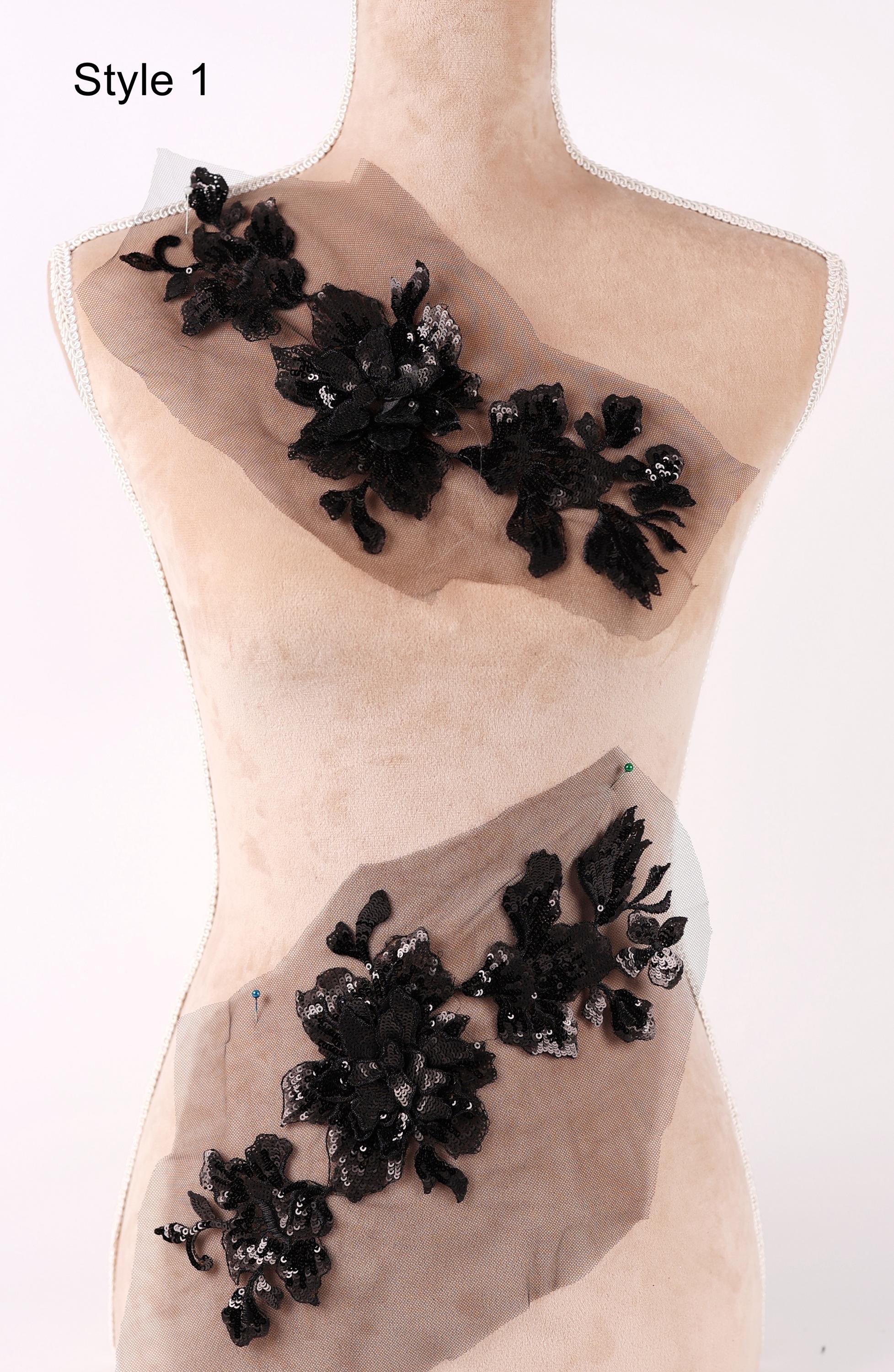 A mannequin wearing a beige dress with black floral embellishments, including a large black flower and smaller black flowers, displayed on the dress.