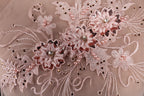 The image is a close-up of a delicate, intricate lace design with pink flowers and sequins.