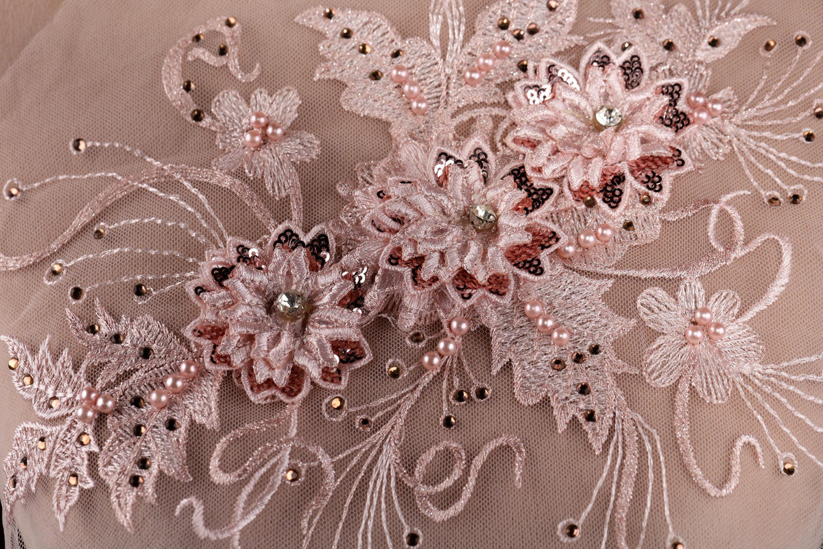 The image is a close-up of a delicate, intricate lace design with pink flowers and sequins.