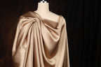 A mannequin wearing a beige satin garment with a draped, flowing design.