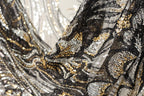 The image is a close-up of a fabric with a black and gold sequin pattern, featuring a mix of black, white, and gold sequins.