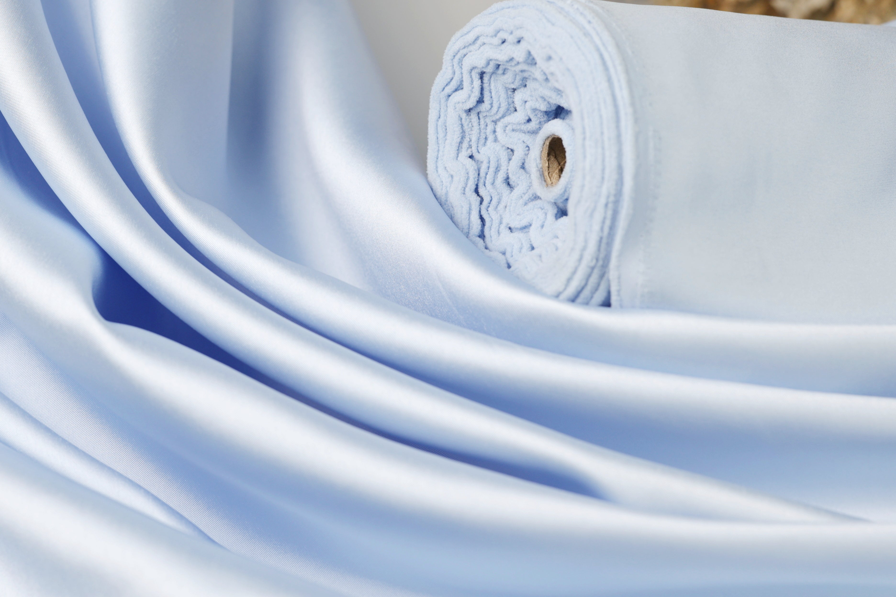 A close-up view of a light blue satin fabric, with its folds and creases visible.