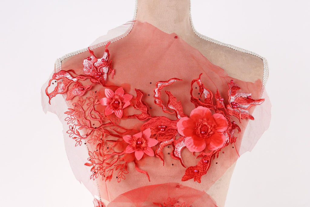 A mannequin wearing a red dress with intricate floral embroidery and lace details.