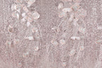 a close-up view of a fabric with a delicate, intricate design of pink and white flowers and leaves. The fabric appears to be made of sequin material, adding a sparkly, textured appearance. The flowers and leaves are arranged in a way that creates a sense of movement and depth, giving the fabric a three-dimensional effect. The image does not contain any text or other discernible objects, and the focus is solely on the floral design.