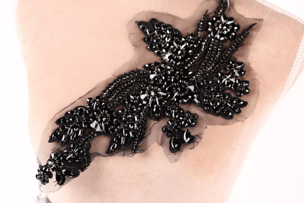 A close-up image of a black, intricate beaded or sequined piece of fabric or accessory, possibly a brooch or embellishment.