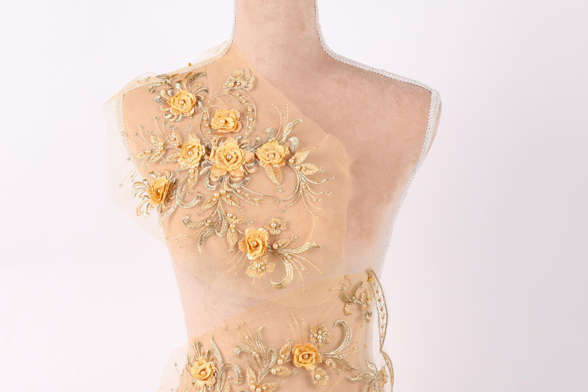 A mannequin with a beige dress adorned with intricate gold and yellow floral embroidery.