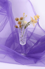 A clear glass vase filled with yellow flowers sits on a purple fabric background.