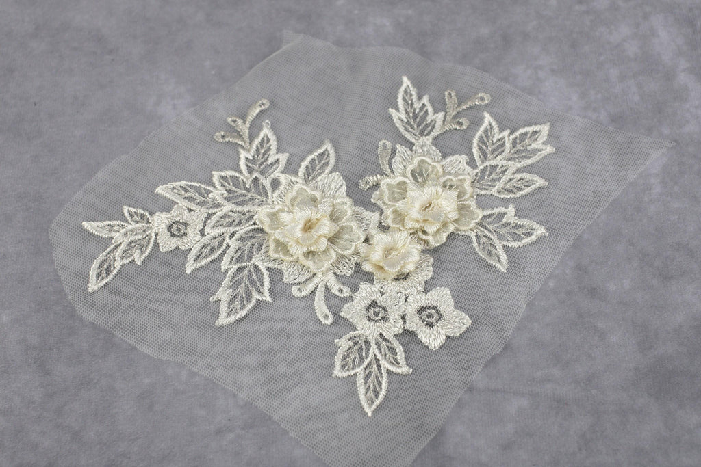 a delicate piece of white lace with intricate floral embroidery, including flowers and leaves, set against a gray background.