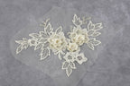 a delicate piece of white lace with intricate floral embroidery, including flowers and leaves, set against a gray background.