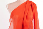 A mannequin wearing a bright orange one-shoulder dress with a draped, flowing fabric.