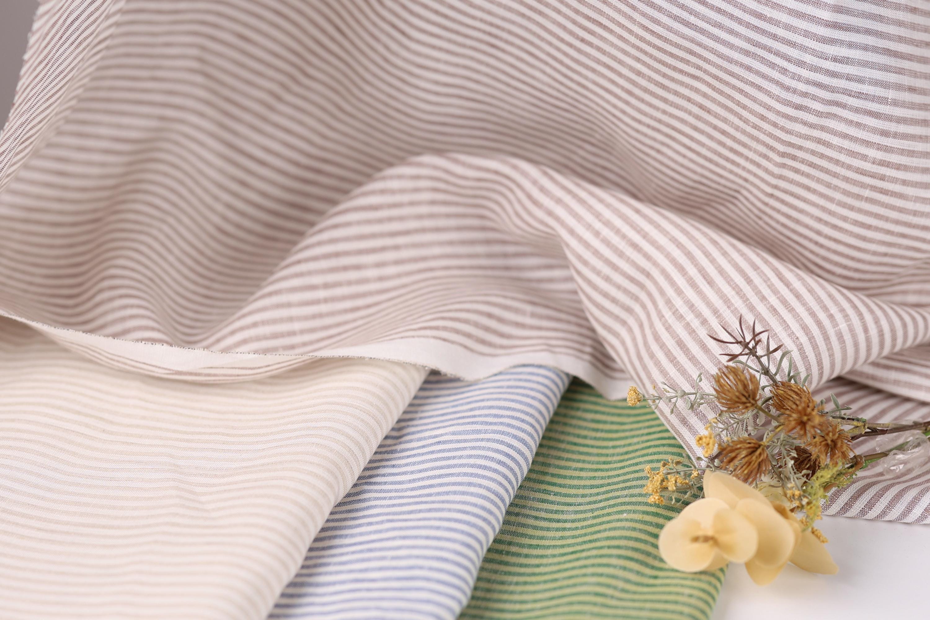 a close-up view of a fabric with horizontal stripes in various colors, including white, beige, blue, and green. A small bouquet of yellow flowers is placed next to the fabric, adding a natural element to the composition.