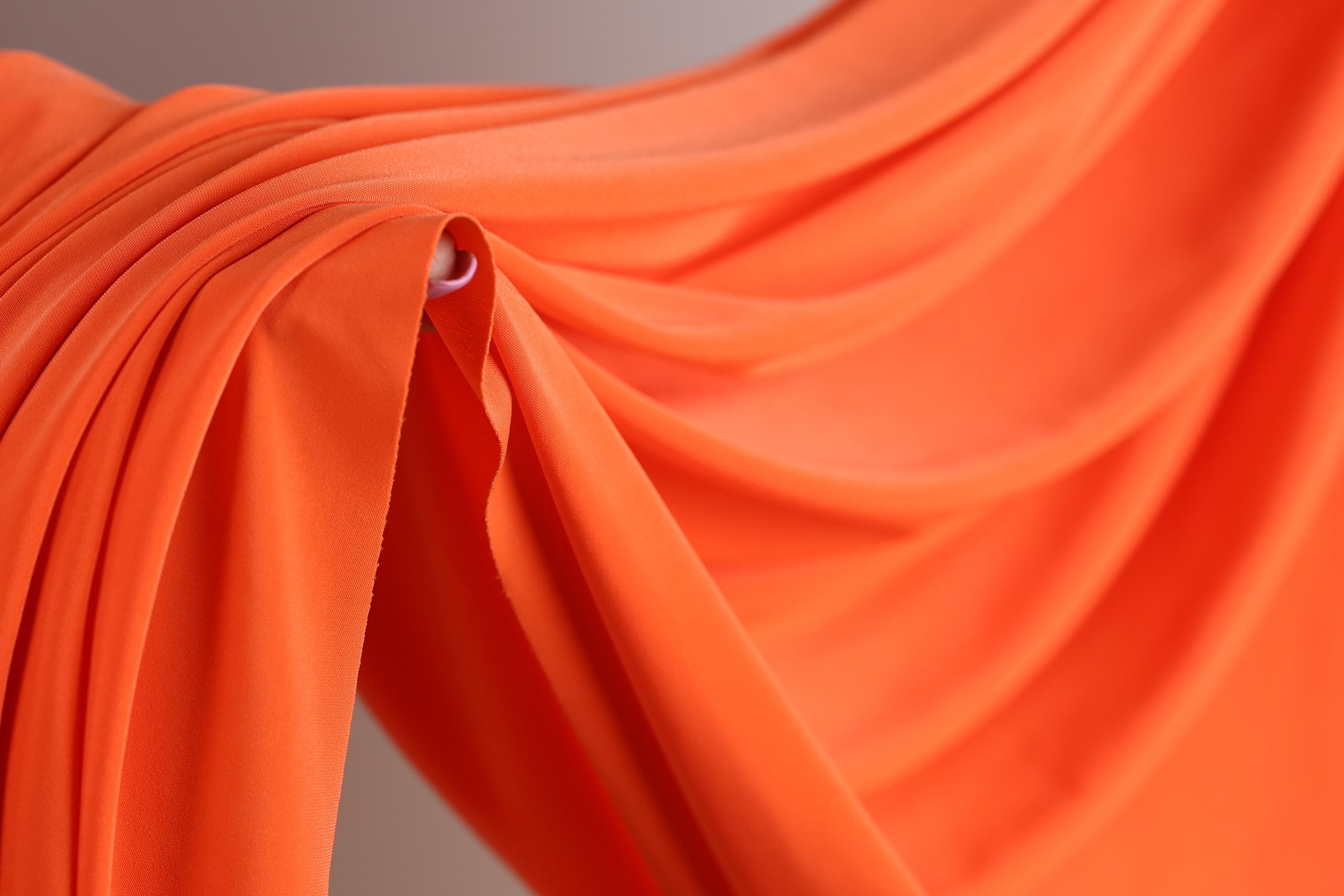 a close-up view of a vibrant orange fabric, with its folds and creases creating a sense of movement and texture.