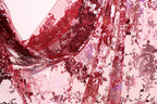 a close-up view of a fabric with a red and pink floral pattern, with a shiny, sequined texture.