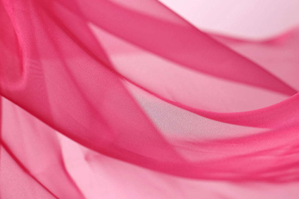 A close-up view of a flowing, pink fabric, possibly silk or chiffon, with a soft, blurred texture.