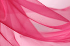 A close-up view of a flowing, pink fabric, possibly silk or chiffon, with a soft, blurred texture.