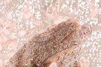 A close-up view of a delicate, intricately beaded fabric with a soft, pastel pink hue.