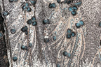 a close-up view of a fabric with a floral pattern, including blue and green leaves and flowers. The fabric appears to be made of sequin material, creating a textured and visually striking appearance.