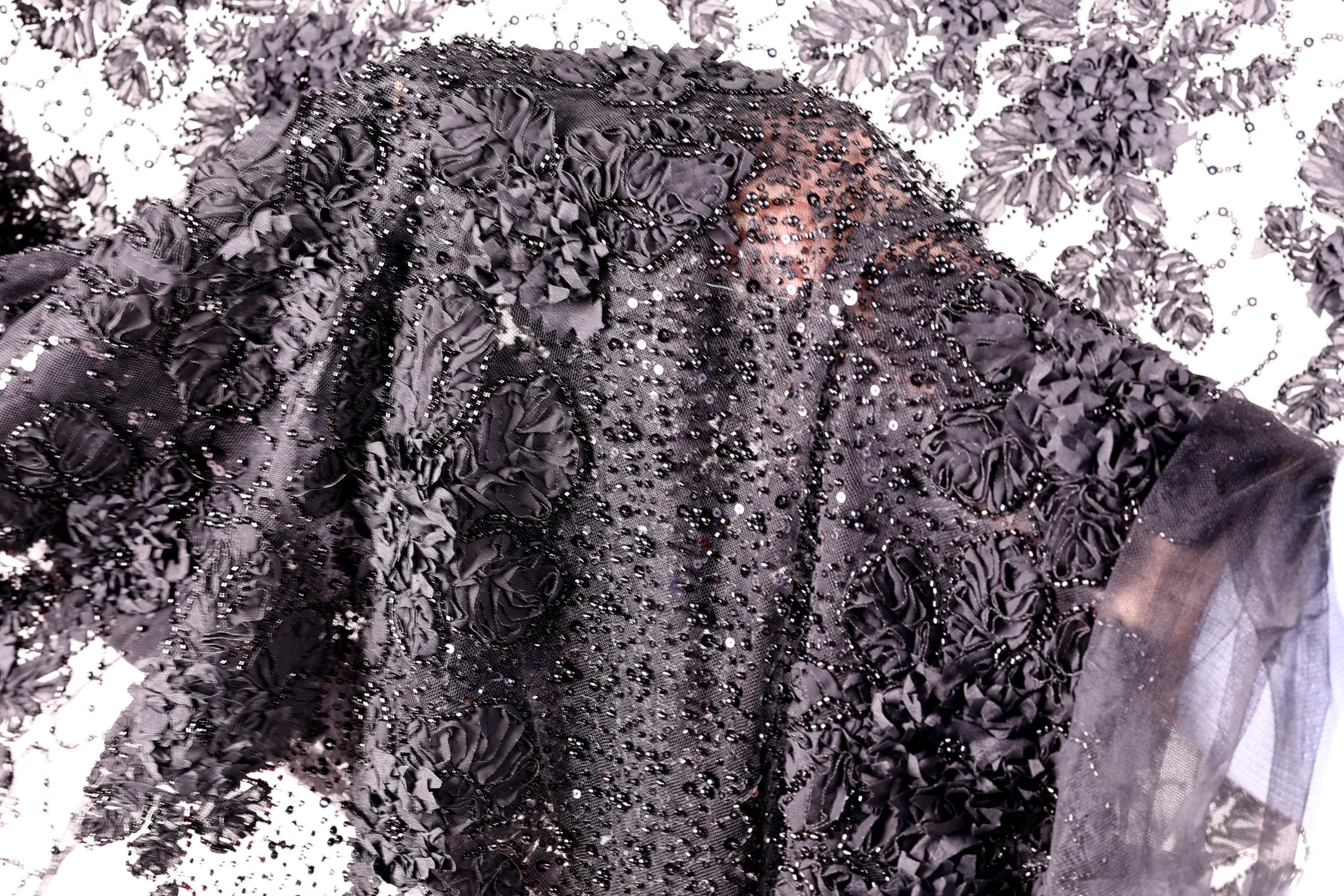 a close-up view of a black fabric with a floral pattern, including black flowers and sequins. The fabric appears to be a black dress or garment with a detailed, intricate design.