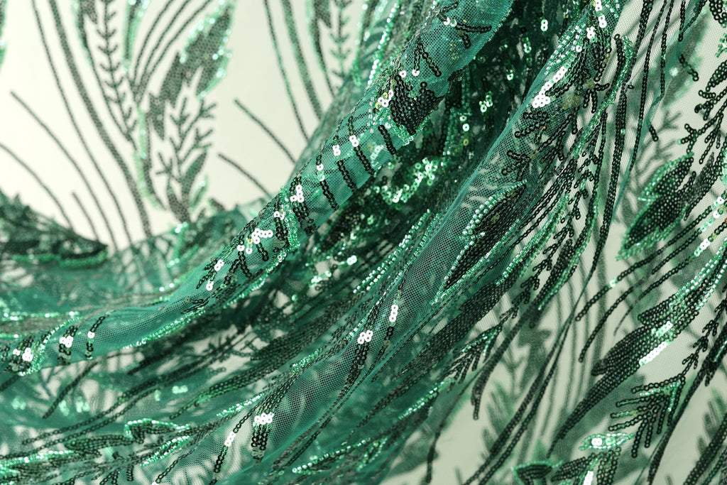 The image is a close-up view of a fabric with a green sequin pattern, featuring a repeating design of green leaves and lines.