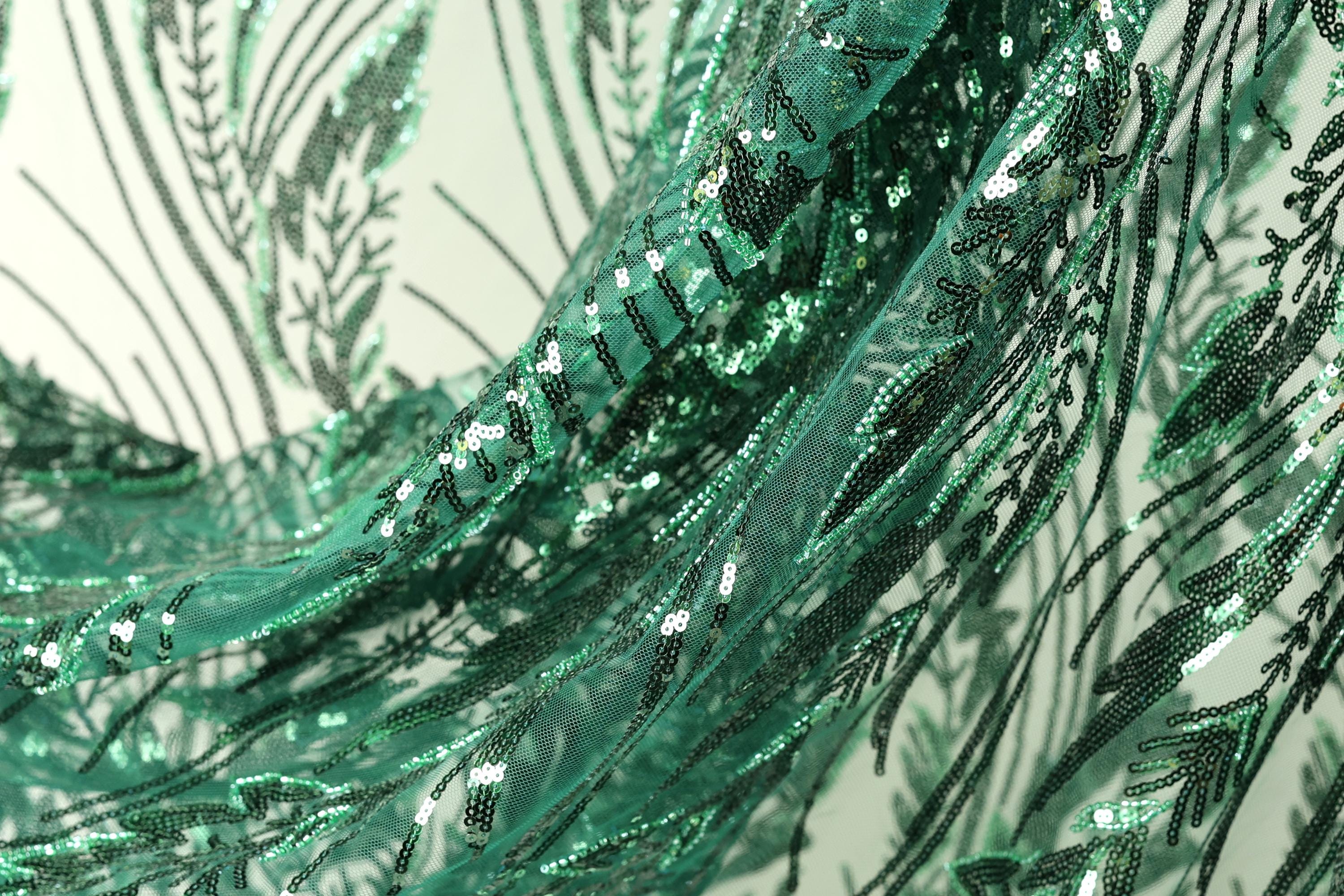 The image is a close-up view of a fabric with a green sequin pattern, featuring a repeating design of green leaves and lines.