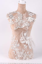 A mannequin wearing a white lace dress with intricate floral and leaf designs.