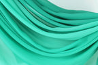 The image is a close-up of a turquoise fabric, with its folds and creases creating a textured and flowing appearance.