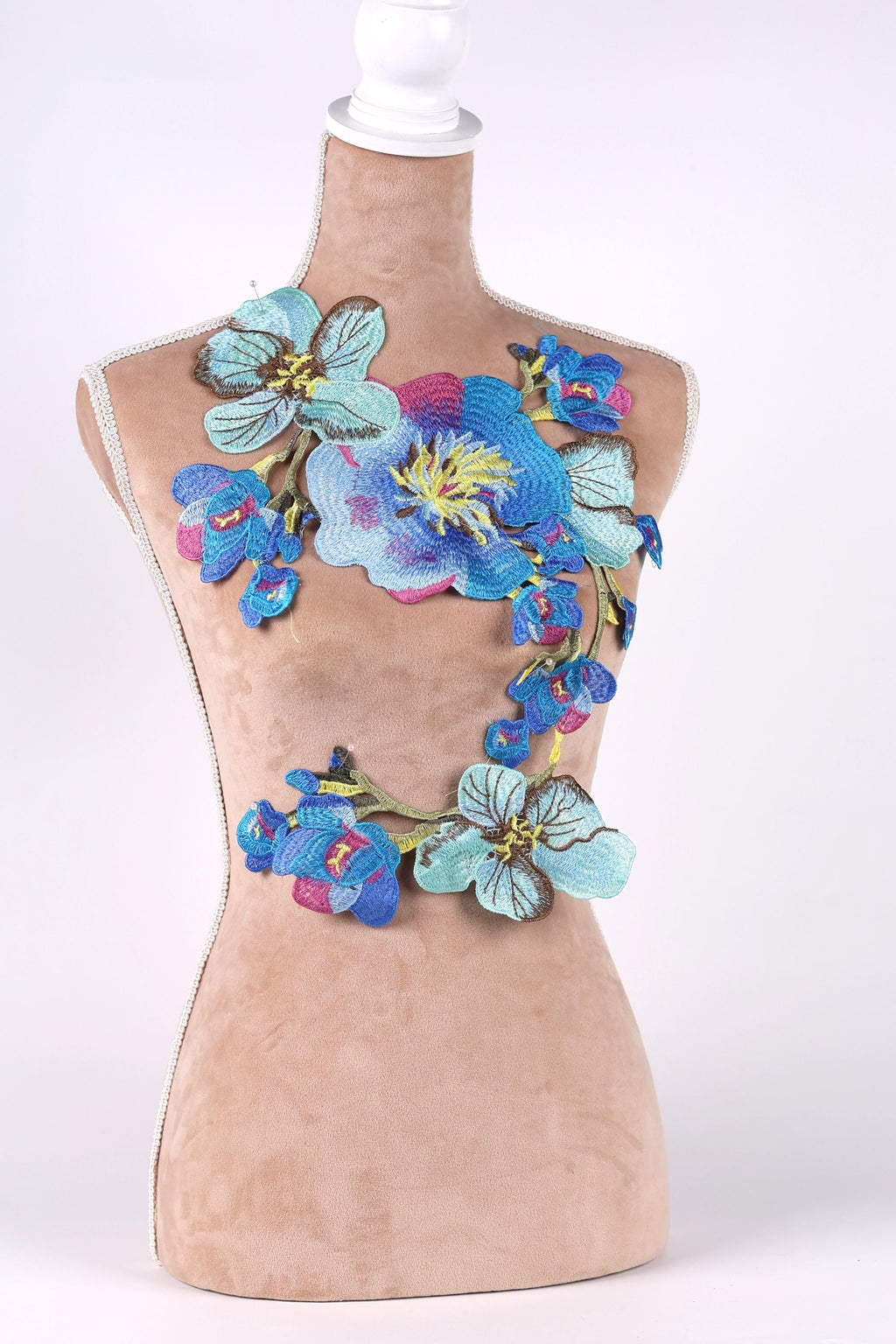 A mannequin bust is adorned with a colorful floral embroidery, featuring blue, pink, and yellow flowers.