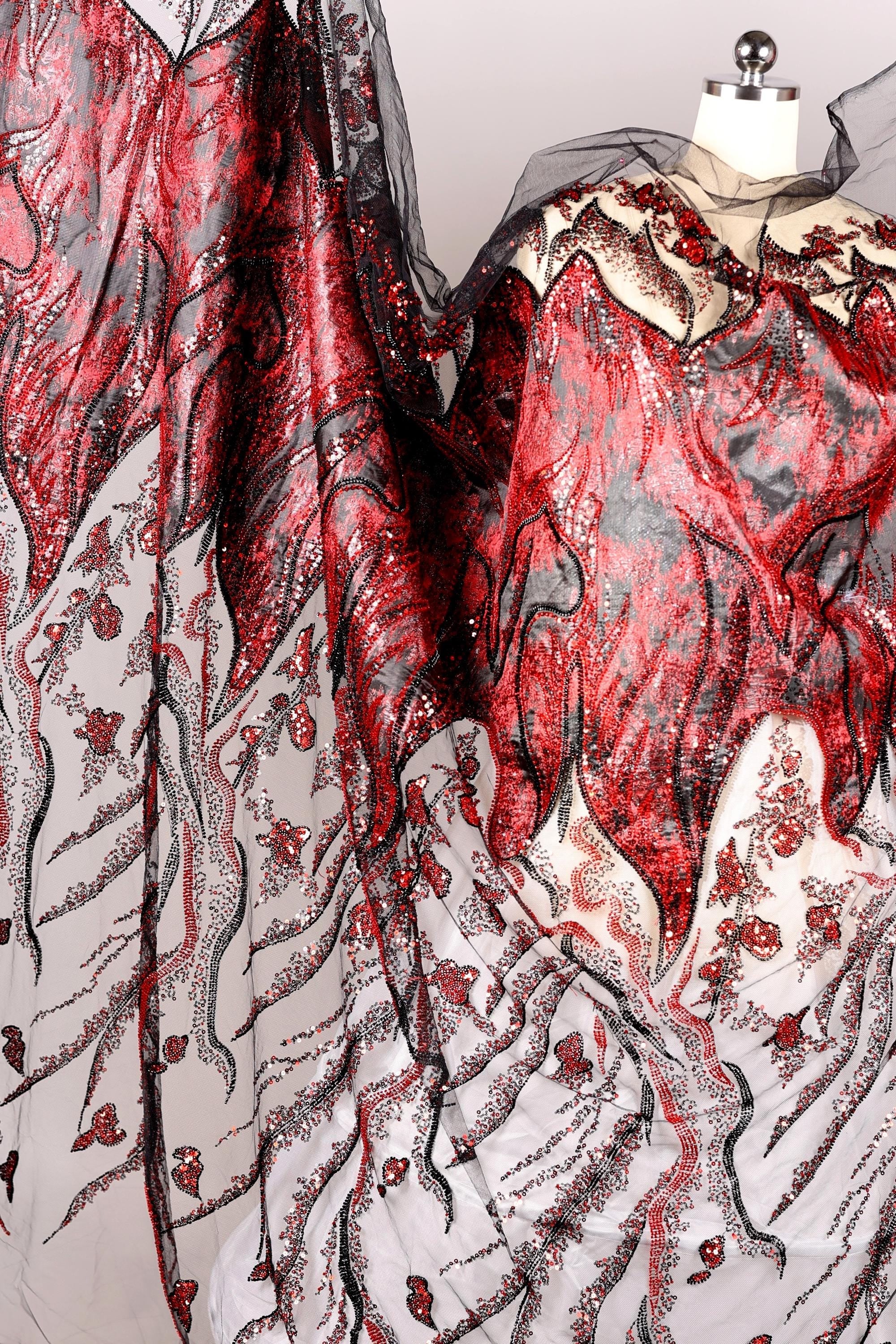 a close-up view of a fabric with a striking red and black pattern, including a mix of sequins and floral designs. The fabric appears to be a sheer material, with a black and white color scheme. The image does not contain any text or other discernible objects or actions.
