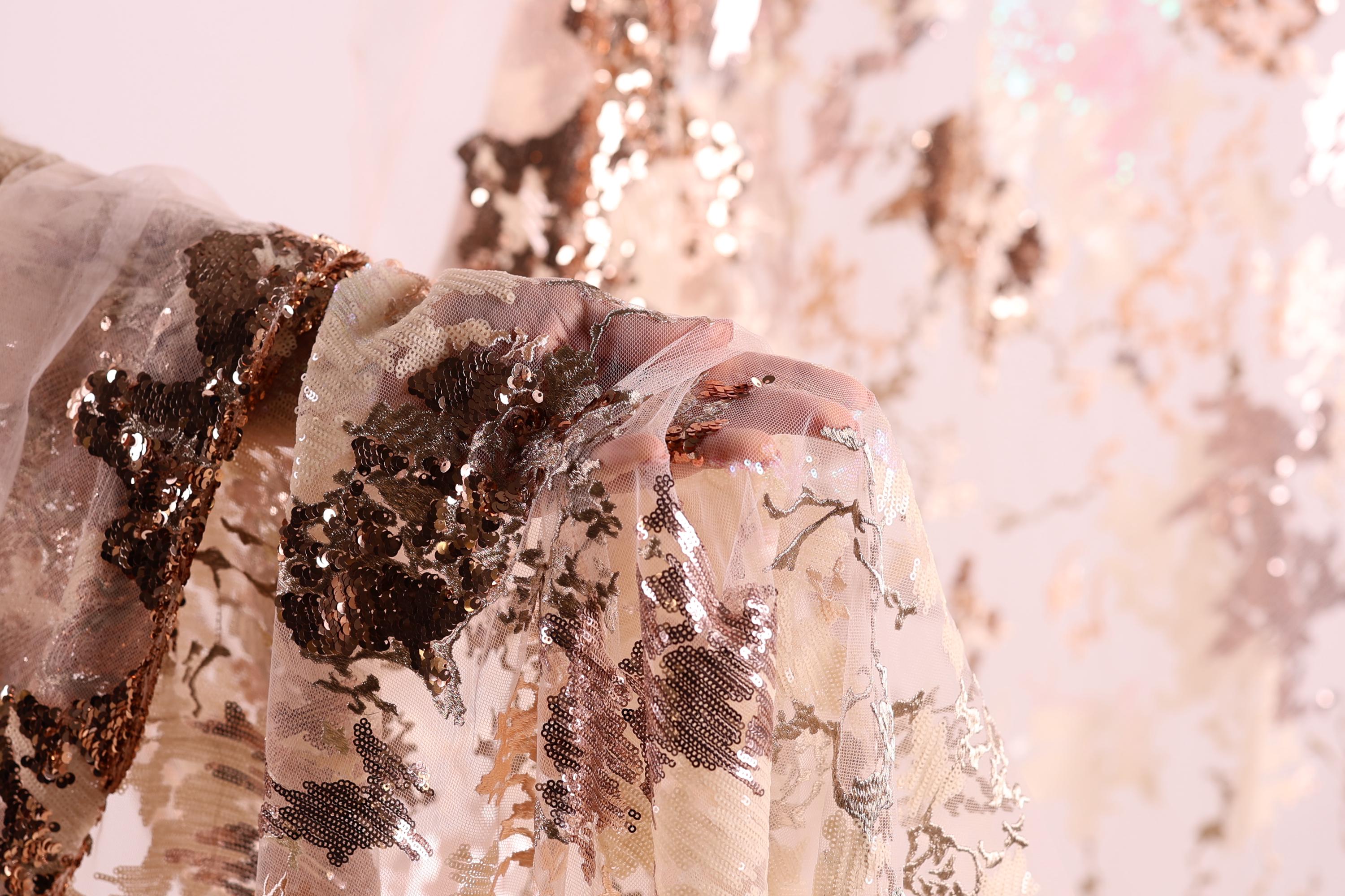 A close-up view of a hand holding a piece of fabric with a floral pattern, featuring a mix of brown and white colors.