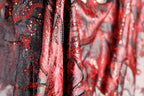 a close-up view of a fabric with a striking red and black pattern, featuring sequins and beads that create a visually captivating design.